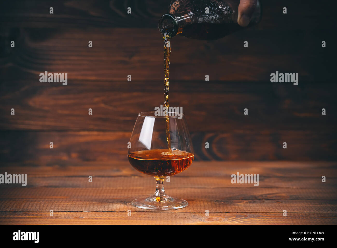 Pouring brandy or cognac from the bottle into the glass against wooden