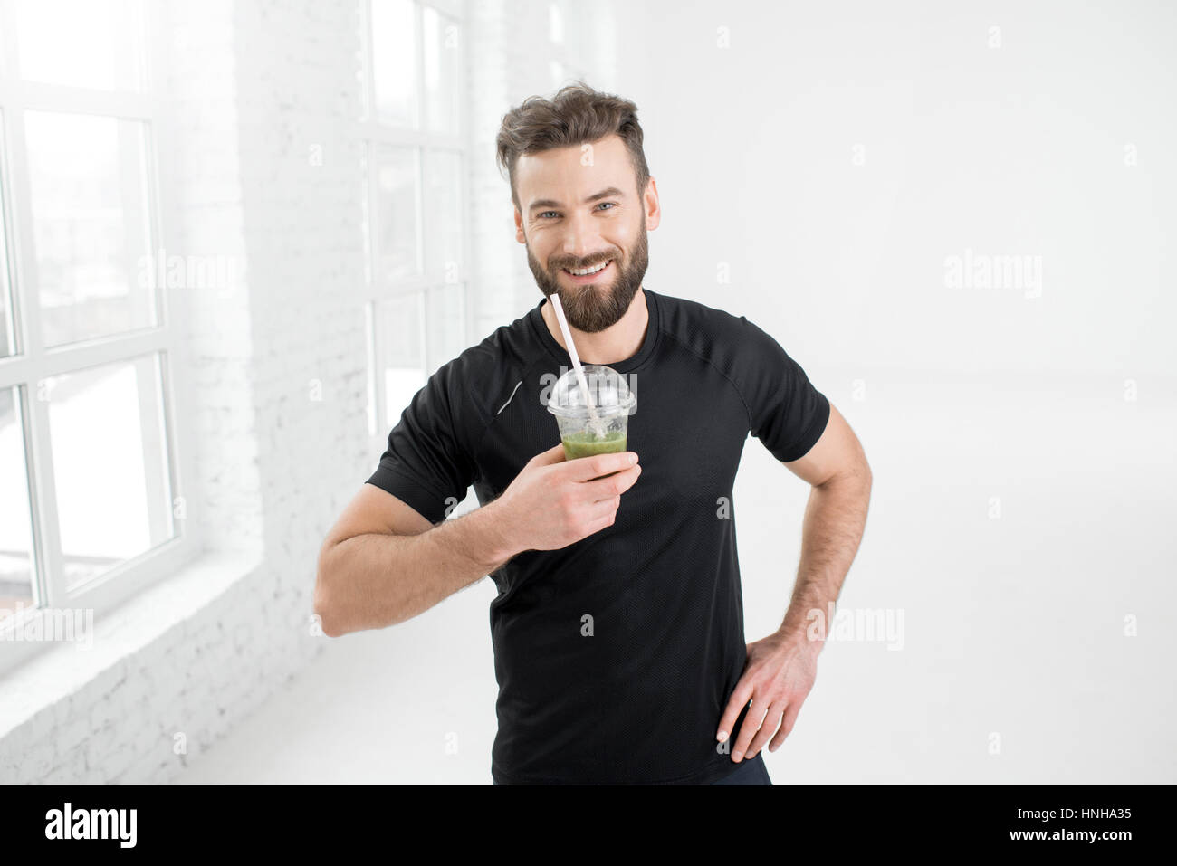 Handsome man in the black sportswear drinking green smoothie in the white gym interior Stock Photo