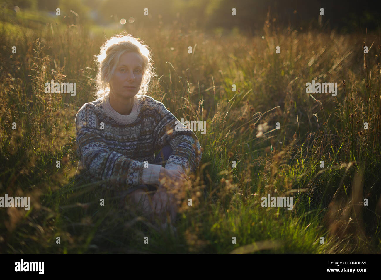 A woman sits in a field at sunset Stock Photo - Alamy