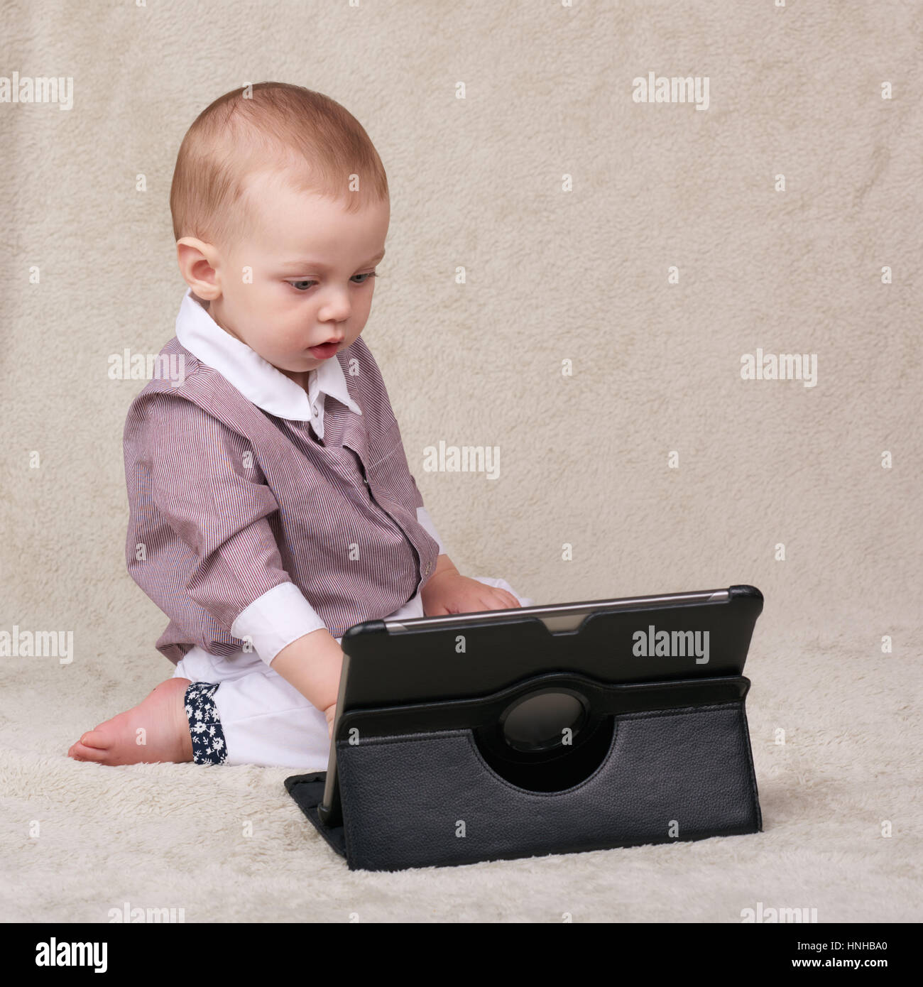 Baby busy using an electronic tablet while sitting on blanket Stock ...