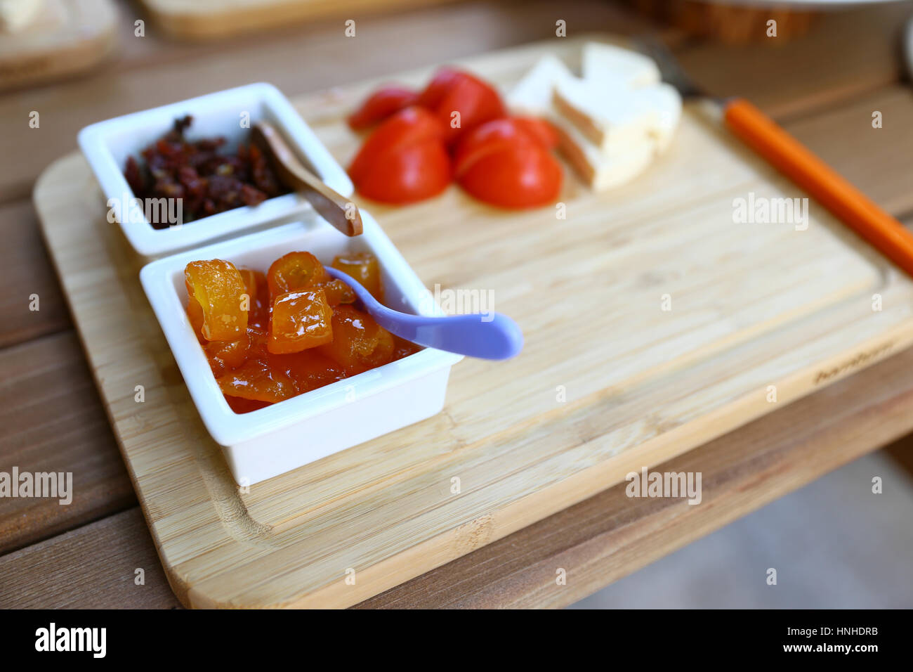 Closeup view of wooden breakfast plate with jam, cheese and tomato, copy space. Stock Photo