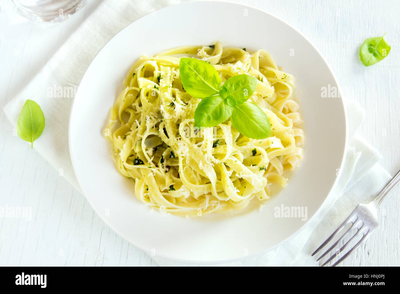 Tagliatelle pasta with pesto sauce, cheese and basil leaves on white