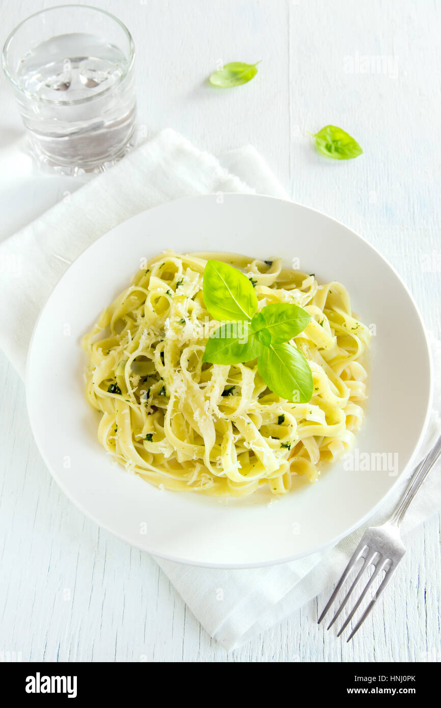 Tagliatelle pasta with pesto sauce, cheese and basil leaves on white