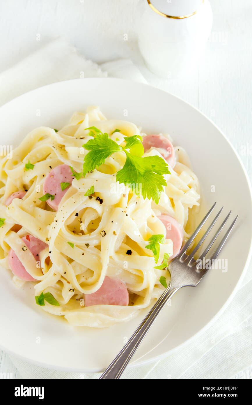 Alfredo tagliatelle pasta with sausages, creamy sauce and greens on