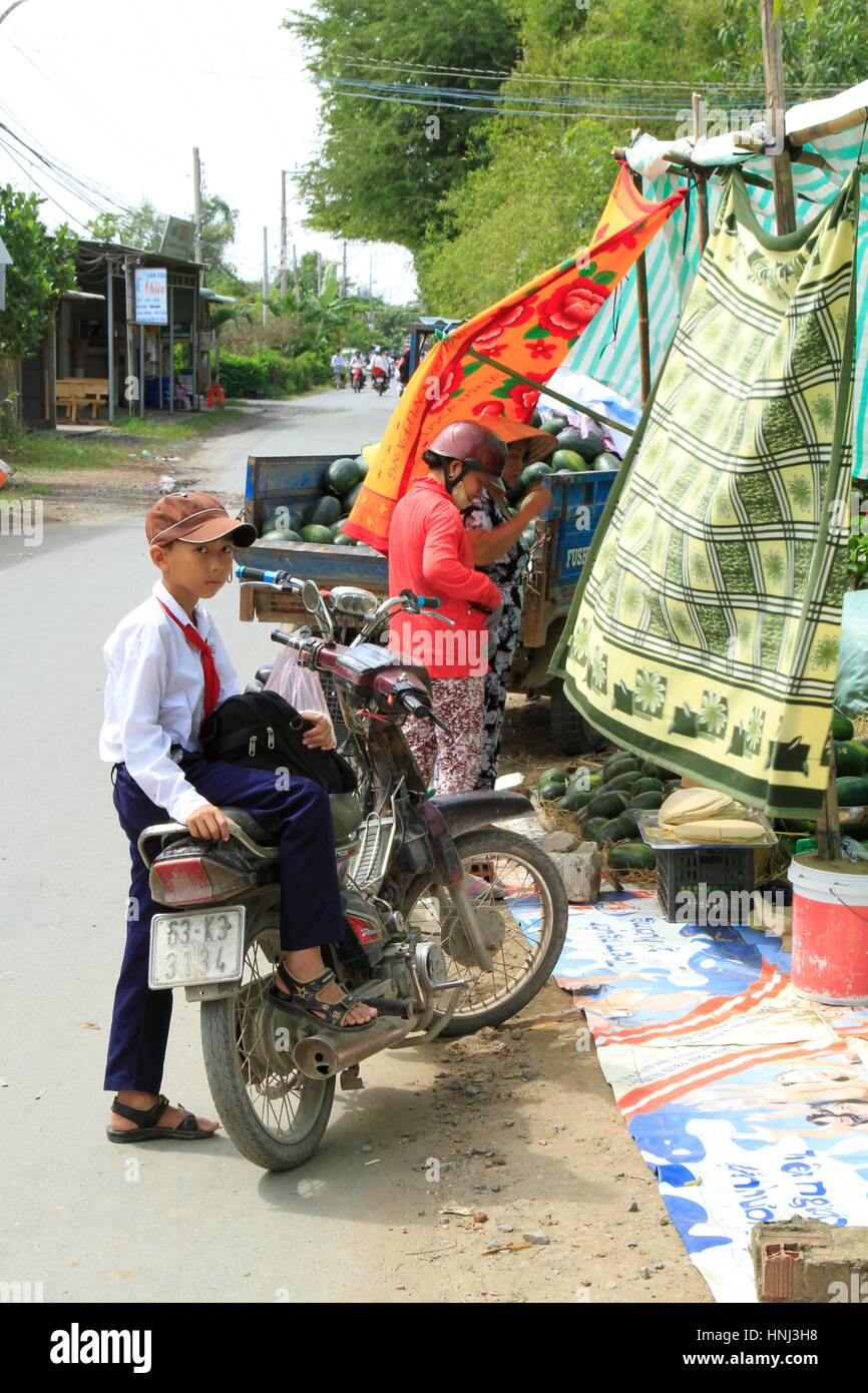 A Vietnamese boy waits for his mom to buy watermelons on the ride home from school. Stock Photo