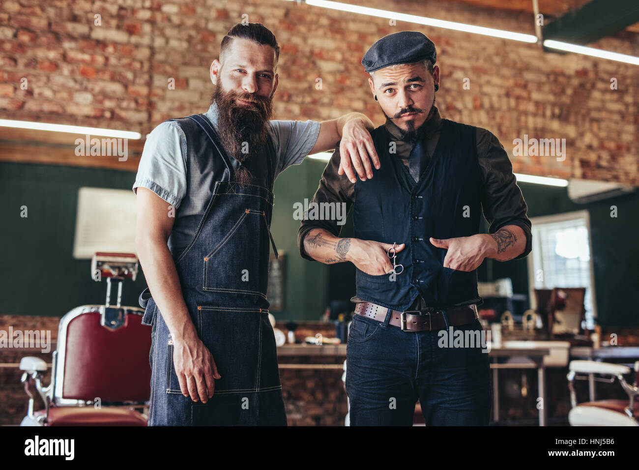 Shot of two stylish man posing together at salon. Barber with client standing at barbershop. Stock Photo