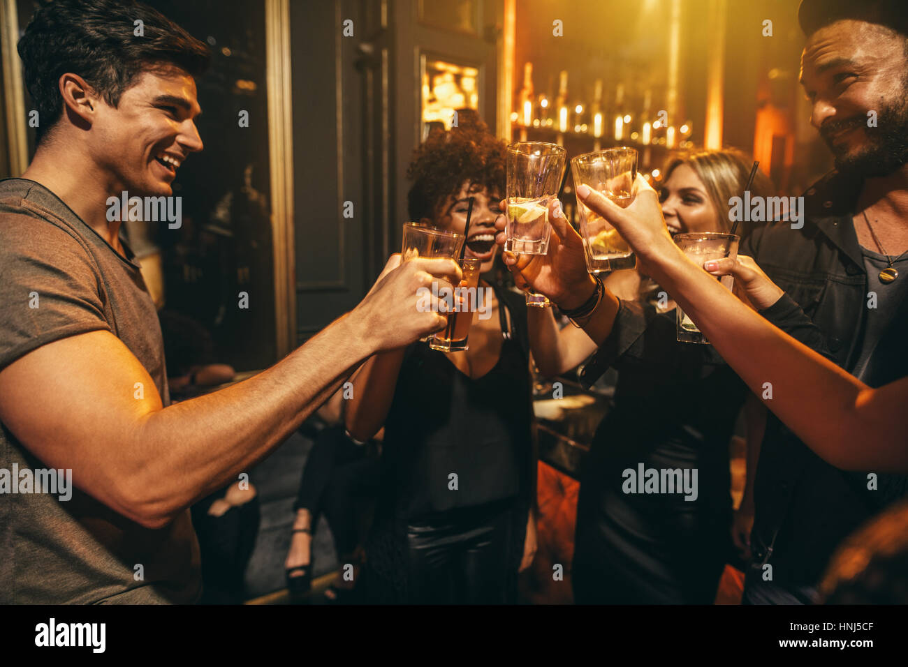 Group of men and women enjoying drinks at nightclub. Young people at bar toasting cocktails and laughing. Stock Photo