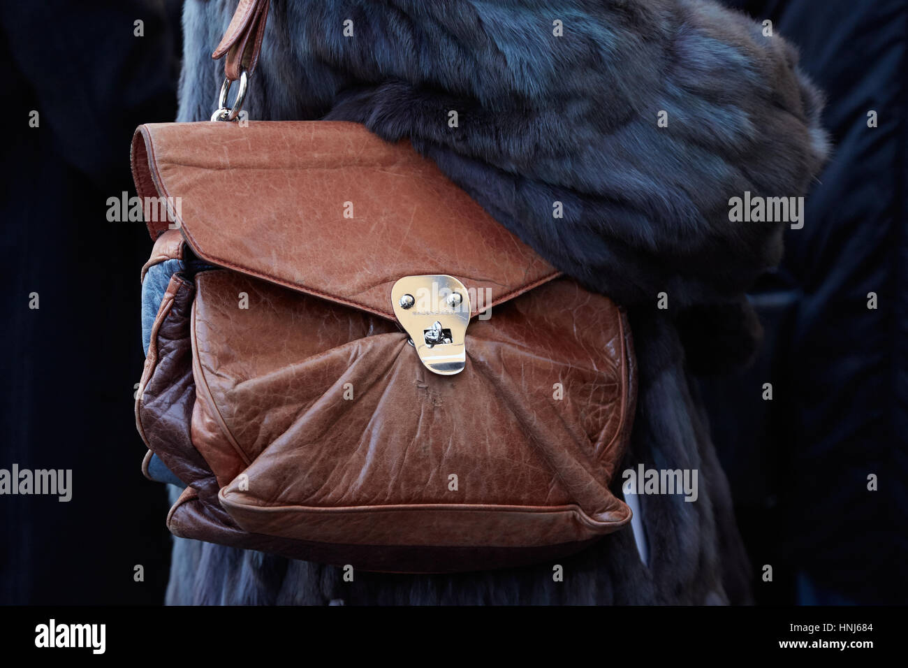 MILAN - JANUARY 16: Woman with Balenciaga brown leather bag and fur coat before Wood Wood fashion show, Milan Fashion Week street style on January 16, Stock Photo
