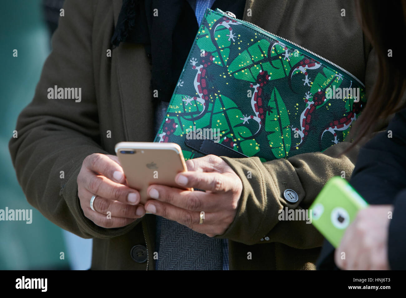 Man with green Furla bag with geckos decoration and iPhone before Emporio Armani fashion show, Milan Fashion Week street style Stock Photo