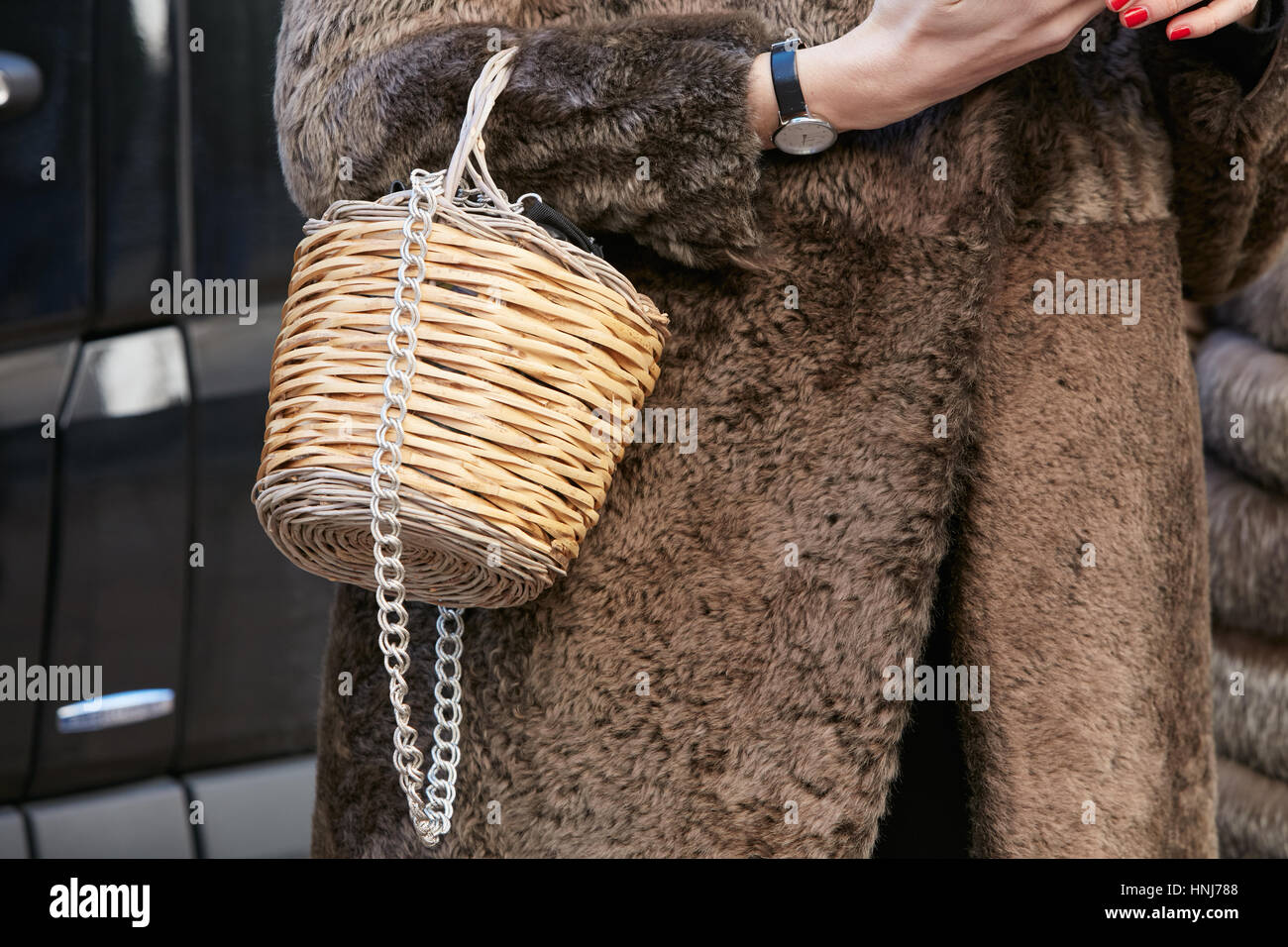 Woman with wicker basket bag and brown fur coat before Salvatore Ferragamo fashion show, Milan Fashion Week street style on January 2017. Stock Photo