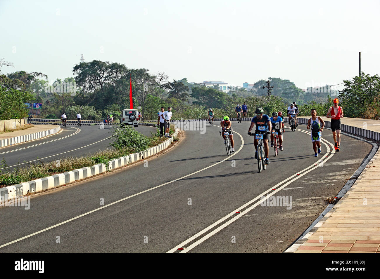 Participants in Goa Triathlon 2017, after finishing swimming part, competing in the running and cycling leg in the scenic highway at Bambolim in Goa Stock Photo