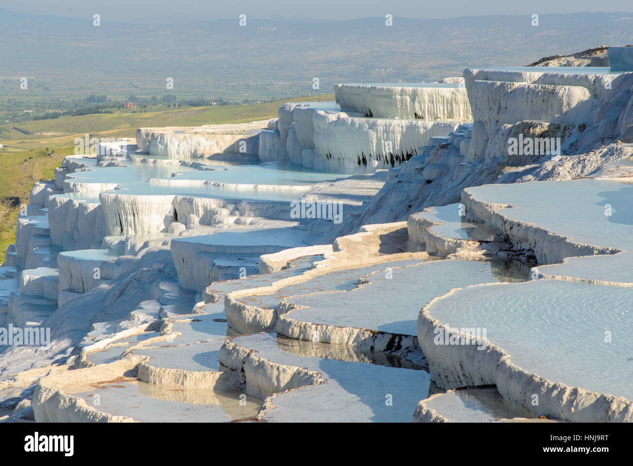 The enchanting pools of Pamukkale in Turkey. Pamukkale contains hot springs and travertines, terraces of carbonate minerals left by the flowing water. Stock Photo