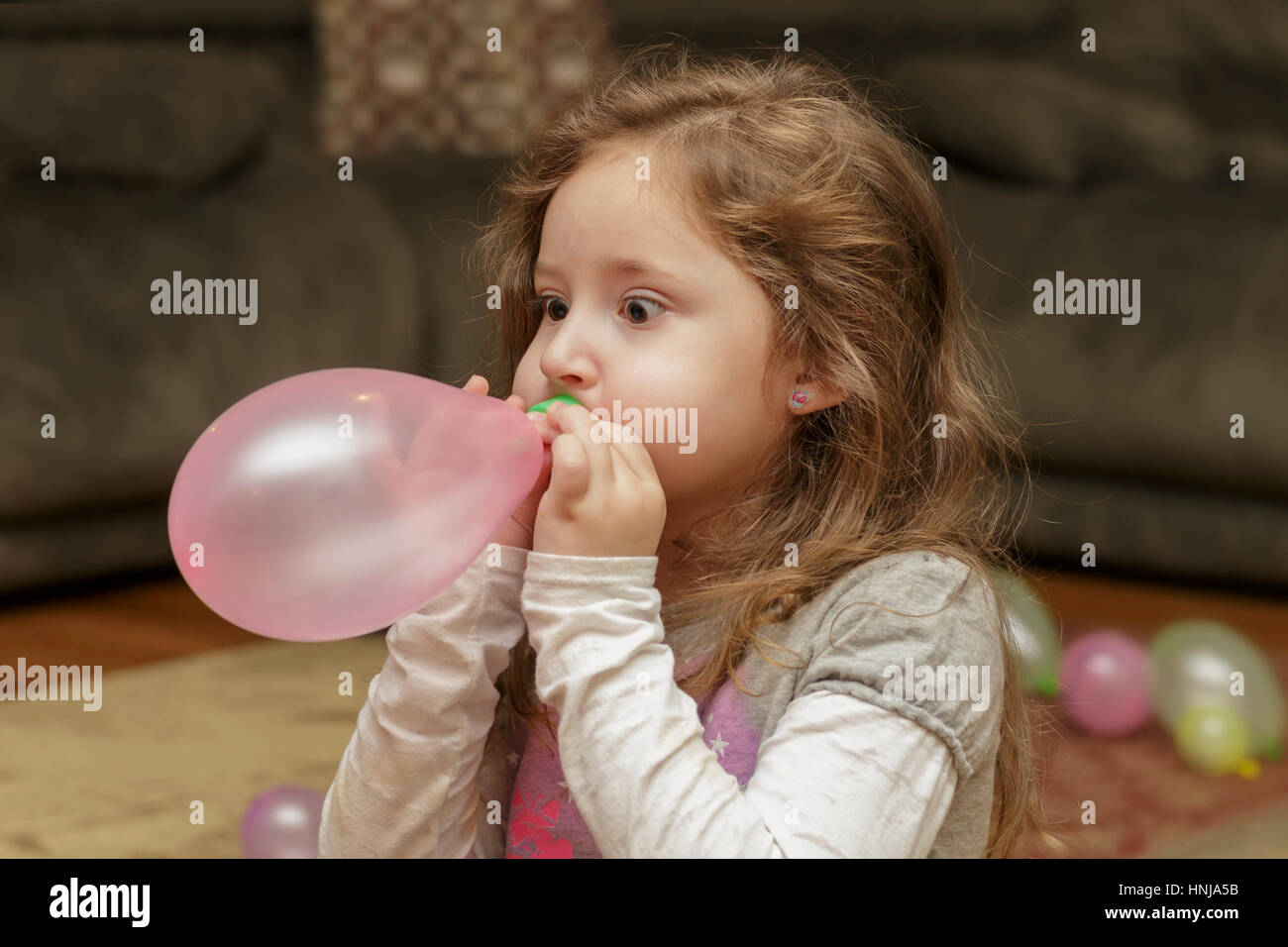 young girl with big eyes blowing up a balloon Stock Photo