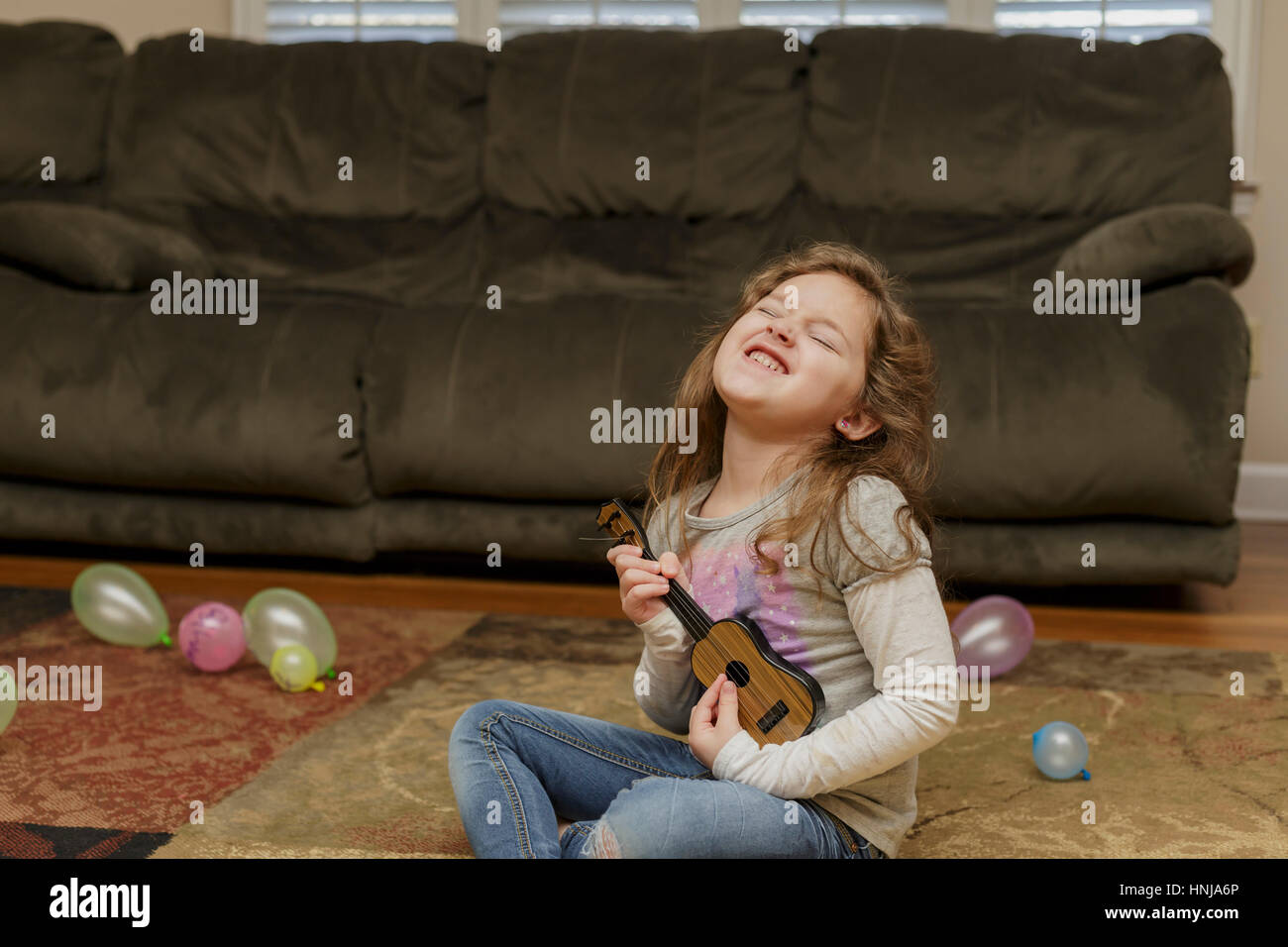 little girl playing a ukulele in her living room floor Stock Photo Alamy