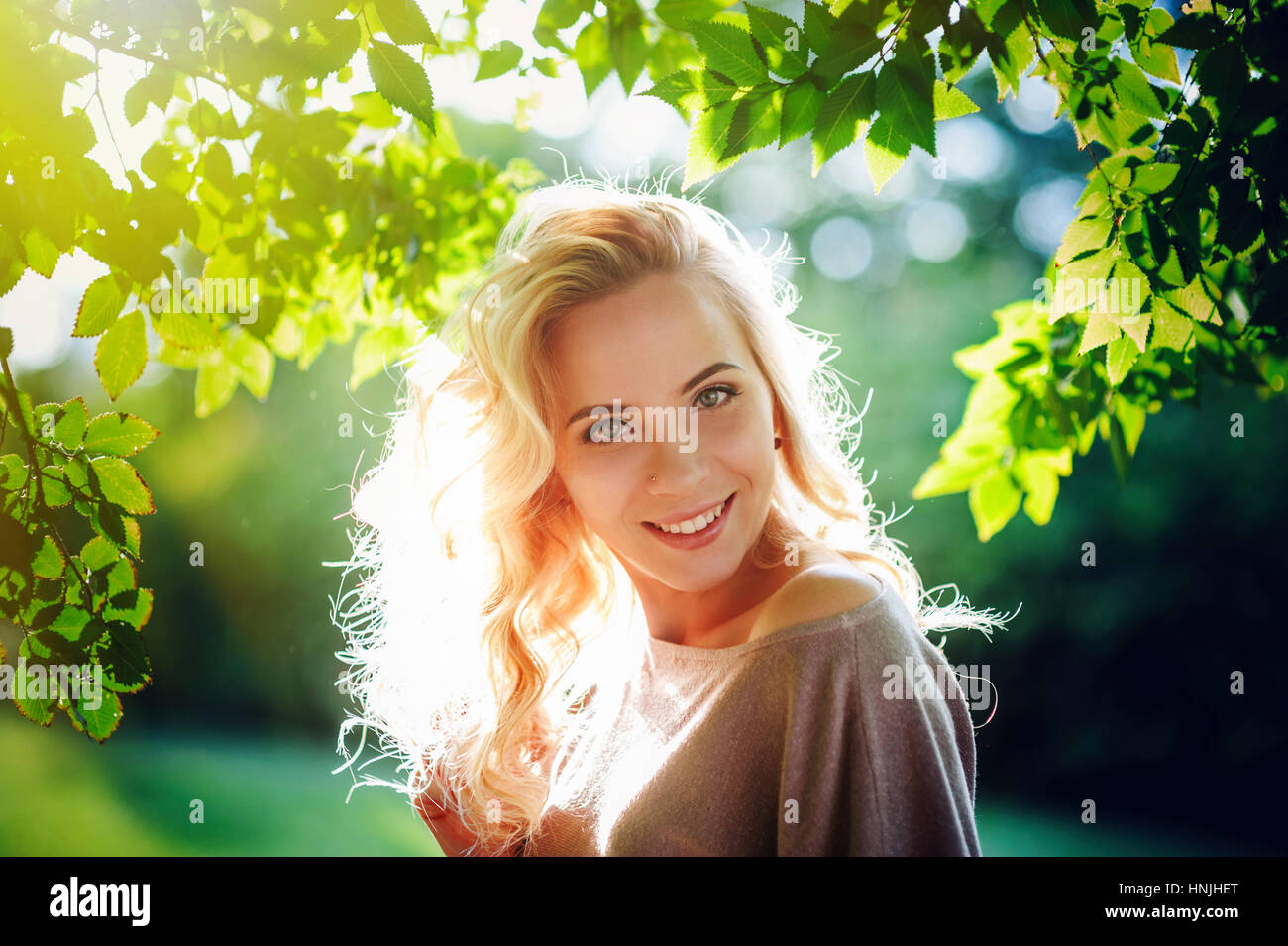 happy young woman illuminated by the setting sun in the park Stock Photo