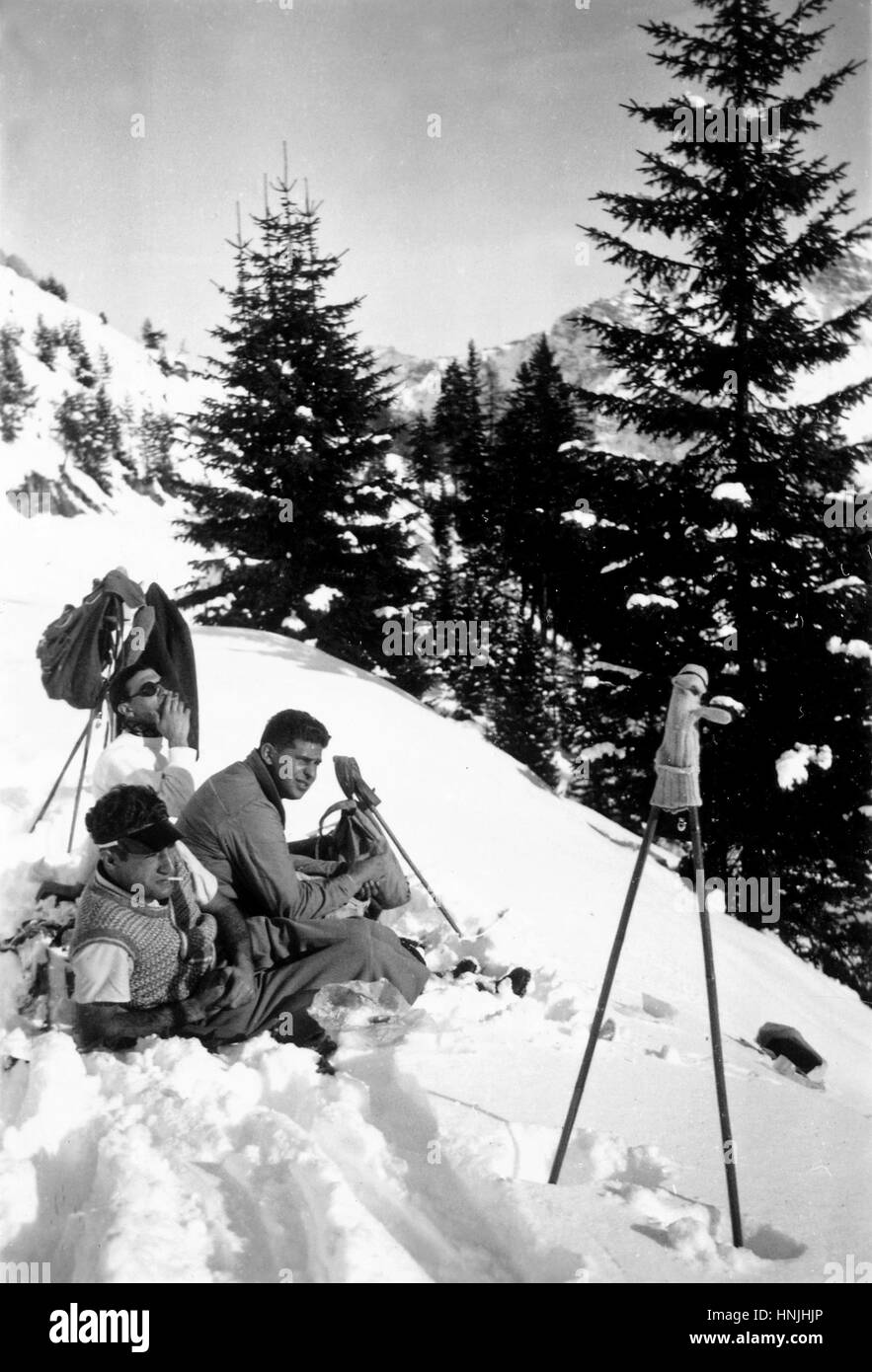 Giau Pass, Italy 1939 - young skiers rest sitting in the snow and smoking a cigarette en route to Giau Pass on Italian Dolomites in winter 1939. Scan from analog photography, private family collection before WWII. Stock Photo