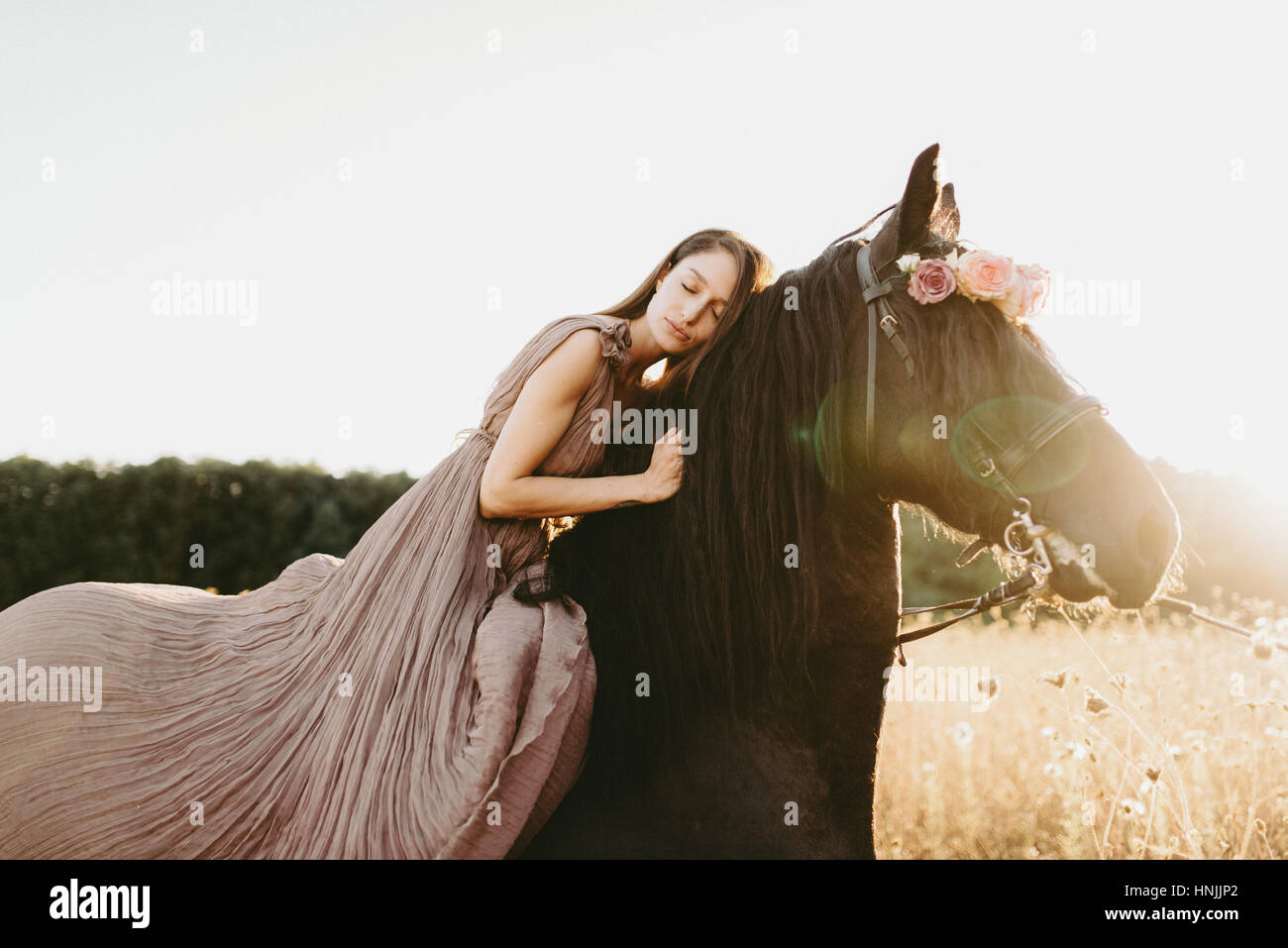 Caucasian woman wearing a beige flowy dress sitting on a black horse, dreaming, contemplating Stock Photo