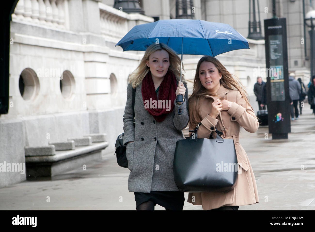 LONDON, UK - APRIL 22, 2016: Two girls under an umbrella on a rainy day cross the road Stock Photo
