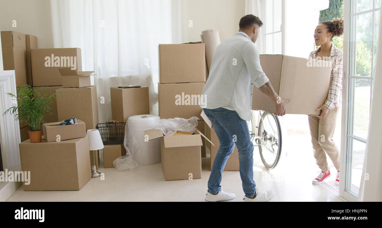 Happy young couple moving into a new house carrying a cardboard box ...