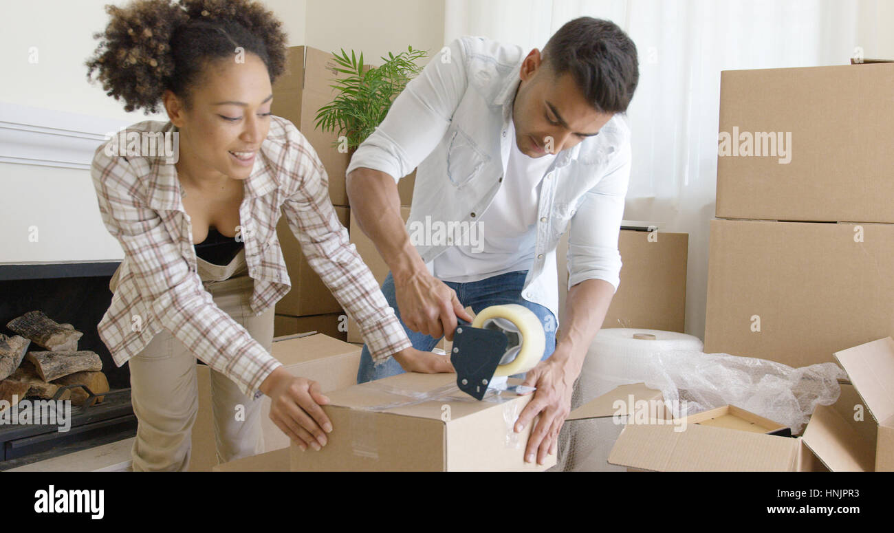 Young couple taping boxes as they pack up their home to move to a new house kneeling together on the floor working as a team Stock Photo