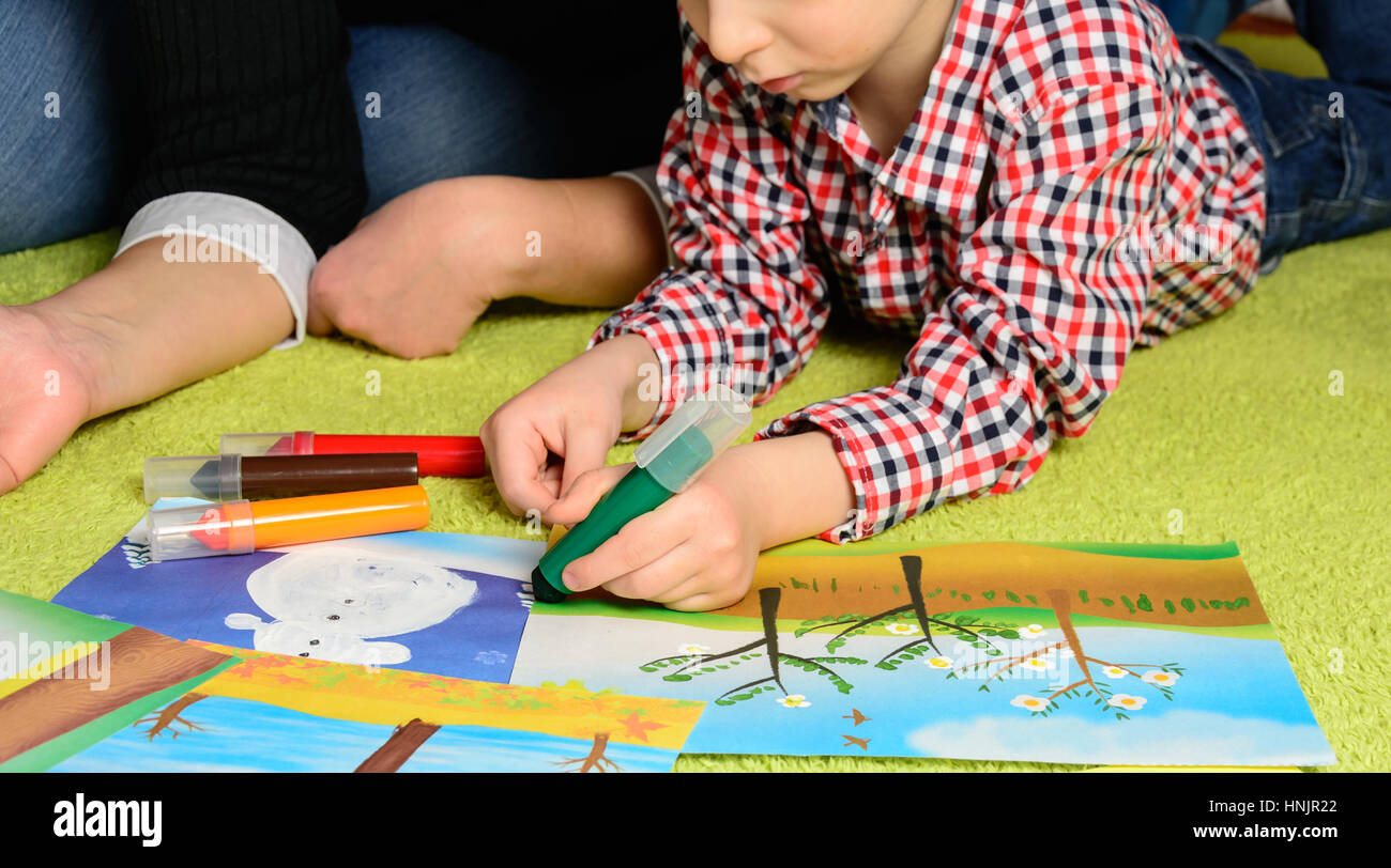 the child together with mother draws a picture lying on a green carpet Stock Photo