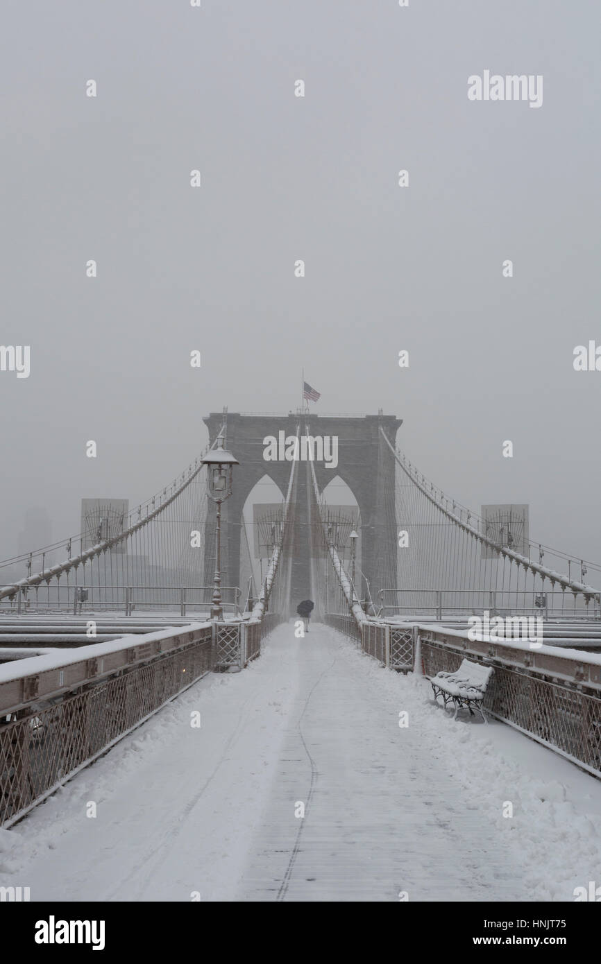 A person walking across New York's Brooklyn Bridge with an umbrella to keep off the snow Stock Photo