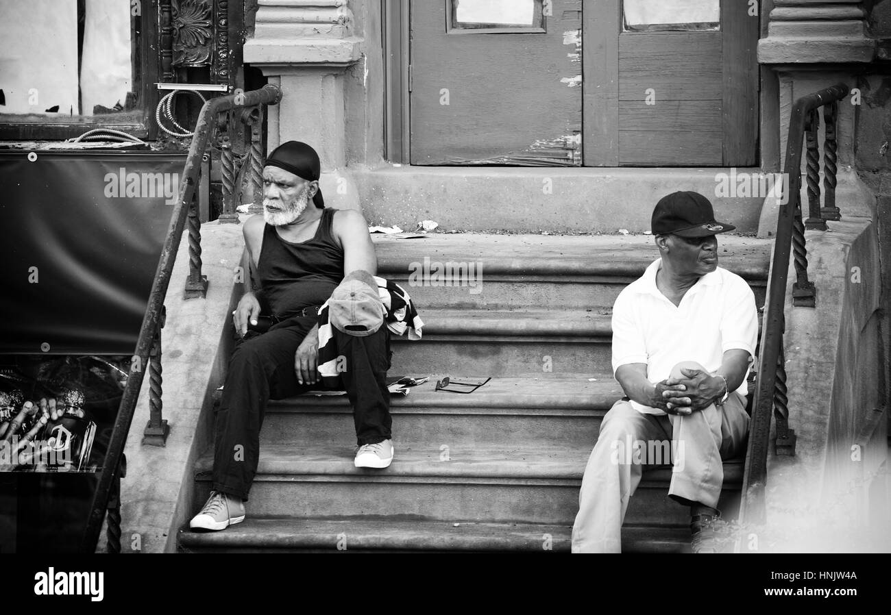Two people sitting on the steps of an entrance of a house in Harlem district Stock Photo