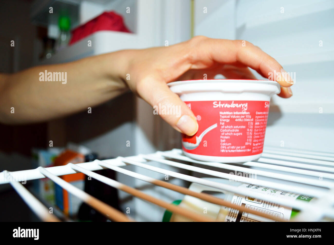 Hand of a woman reaching for a dessert in a fridge. Stock Photo