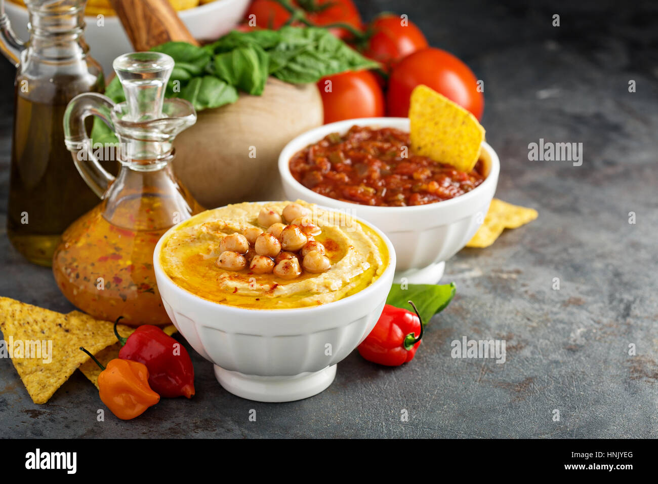 Homemade hummus and tomato salsa in white bowls with vegetables and