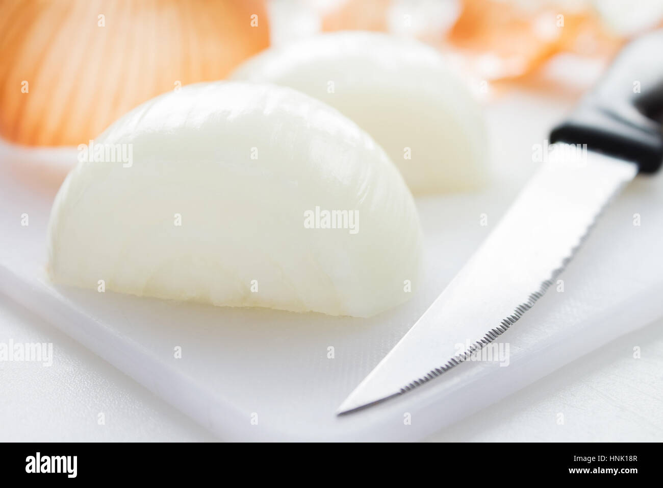 Yellow onion peeled and cut in half on a white chopping board Stock ...