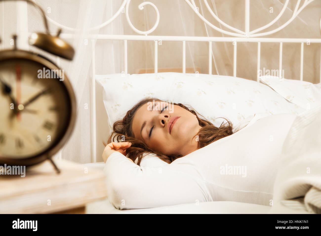 Young woman sleeping in bed beside alarm clock Stock Photo