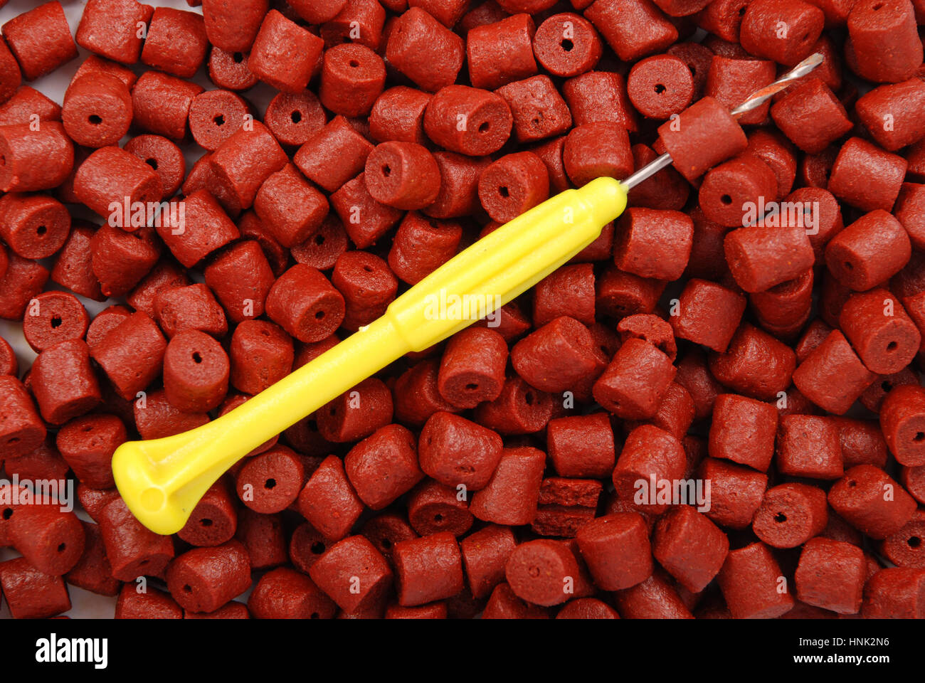 Red pre-drilled halibut pellets for carp fishing and yellow stinger needle background  Stock Photo - Alamy