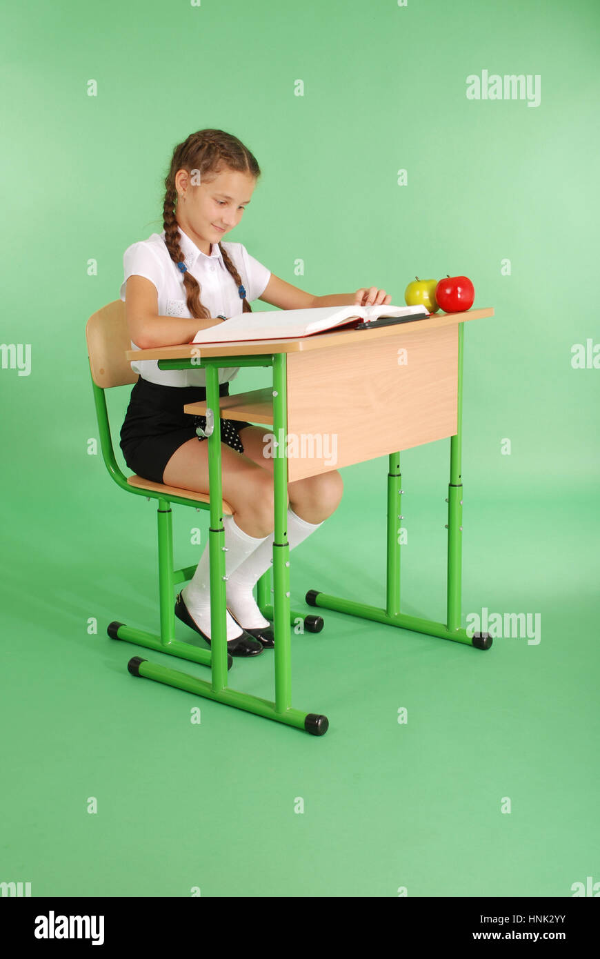 Girl in a school uniform sitting at a desk and reading a book isolated ...