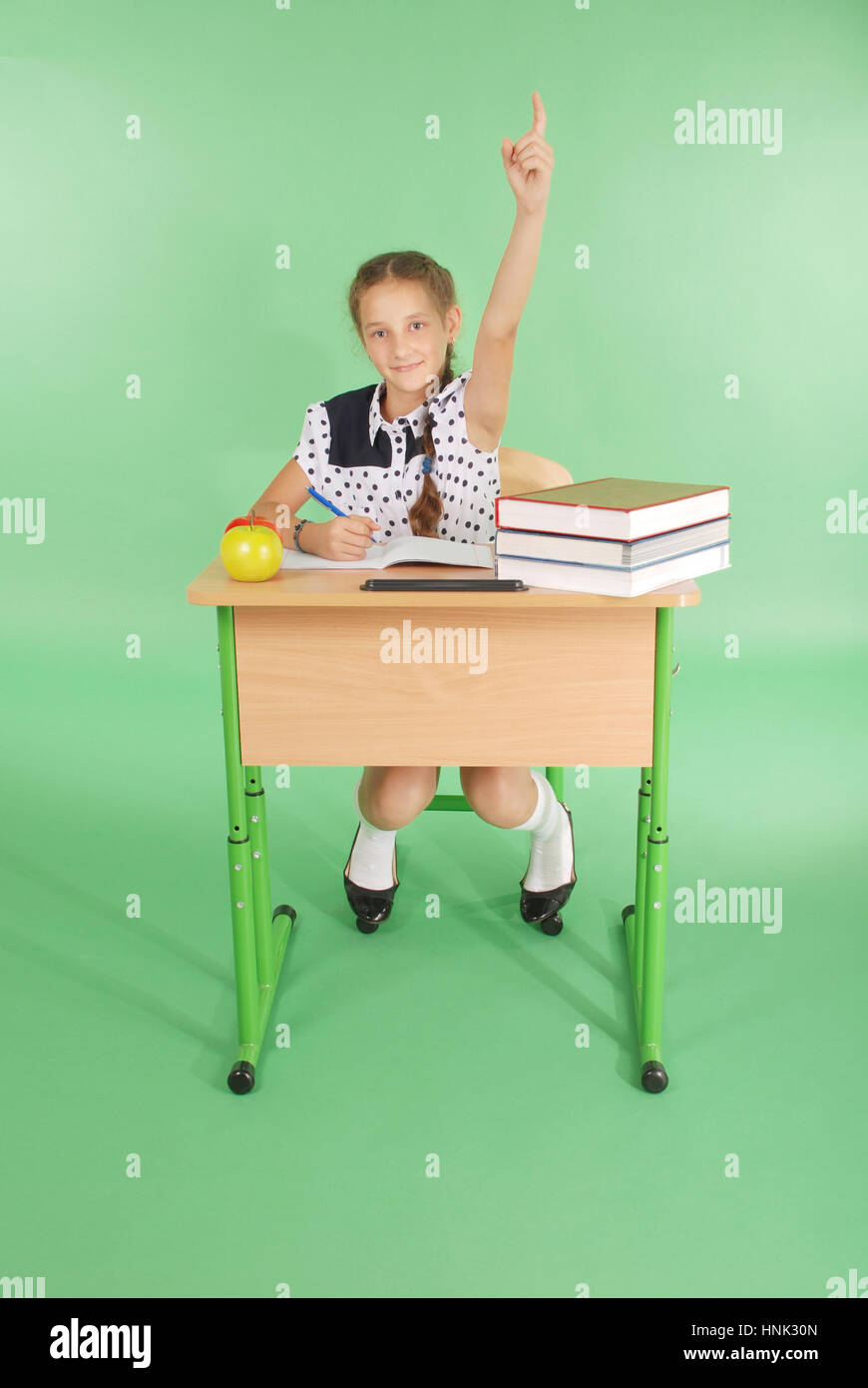 Girl in a school uniform raising hand to ask question isolated on green