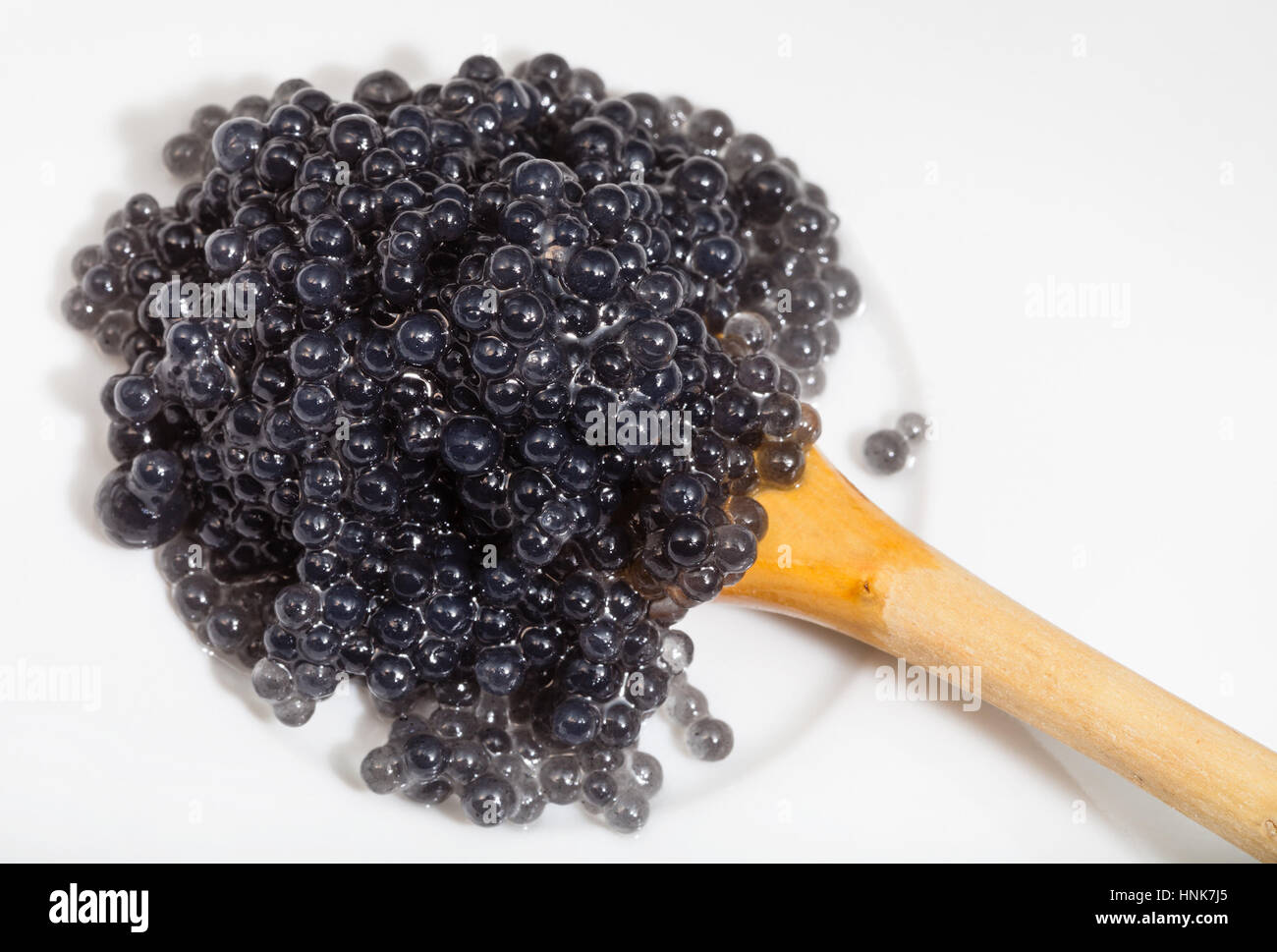 top view of black coloured pickled caviar of halibut fish in wooden spoon on white plate Stock Photo