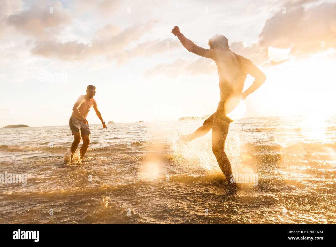 Two people having fun fighting with water splash in the sea with summer sunset, droplets effect and tilted photo to show action Stock Photo