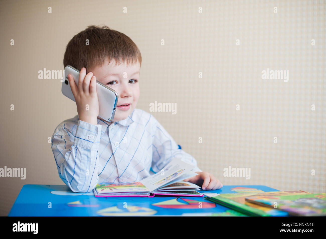 little boy sitting at desk and talking on the phone Stock Photo