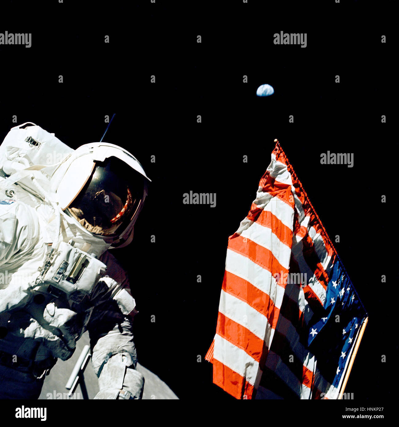 Scientist-astronaut Harrison H. Schmitt stands by the American flag during a moonwalk on the Apollo 17 mission. Home, that small dot in the blackness of space above the flag, is a quarter-million miles away.  Schmitt, Gene Cernan and Ron Evans made the Apollo program's final journey to the moon in December 1972.  Photo Credit: NASA Stock Photo