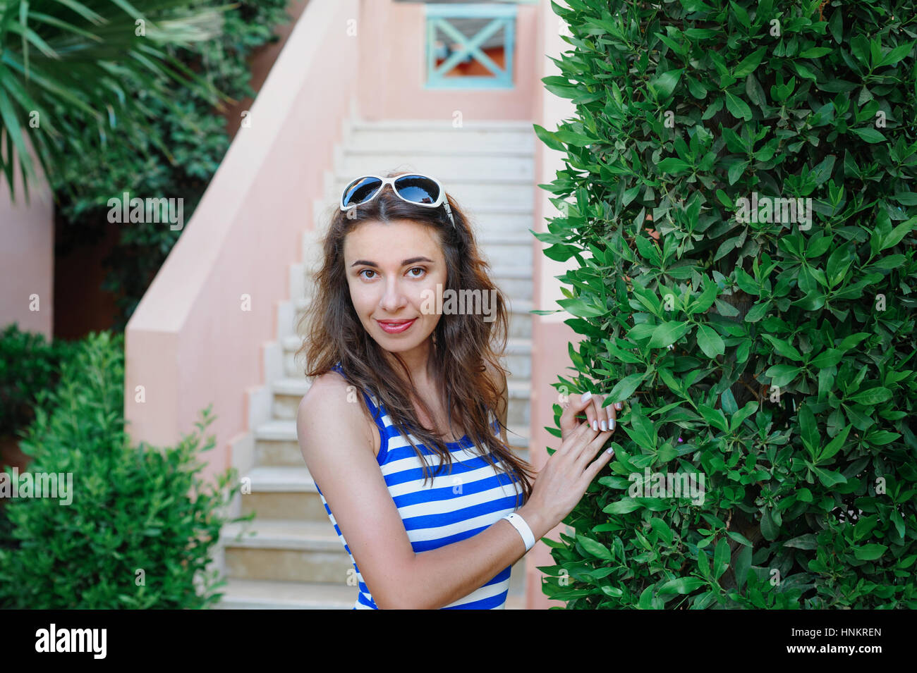 beautiful young woman standing near a green bush in a park Stock Photo