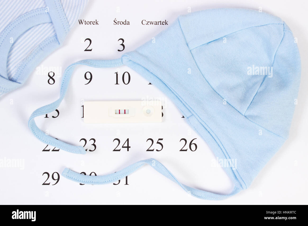 Pregnancy test with positive result and clothing for newborn on calendar with polish inscription, concept of extending family and expecting for baby Stock Photo