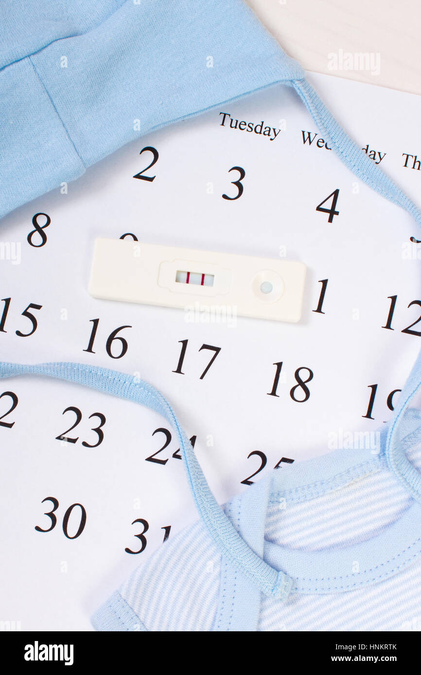 Pregnancy test with positive result and clothing for newborn on calendar, concept of extending family and expecting for baby Stock Photo