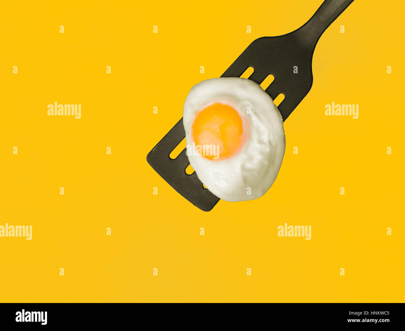 Sunny side up egg on a spatula 3/4-overhead view on yellow background Stock Photo