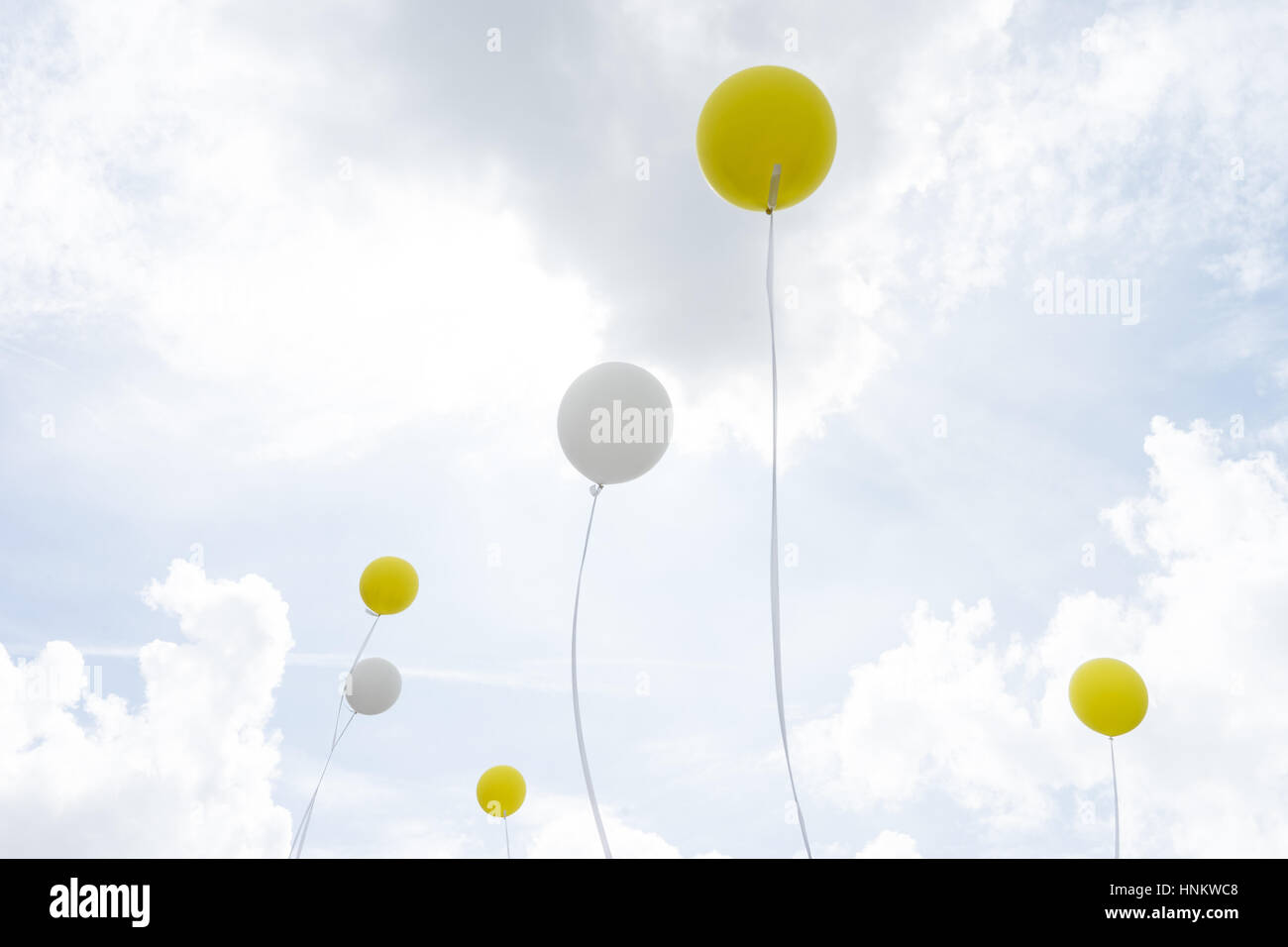 white and yellow helium balloons on a rope with cloudy sky background Stock Photo