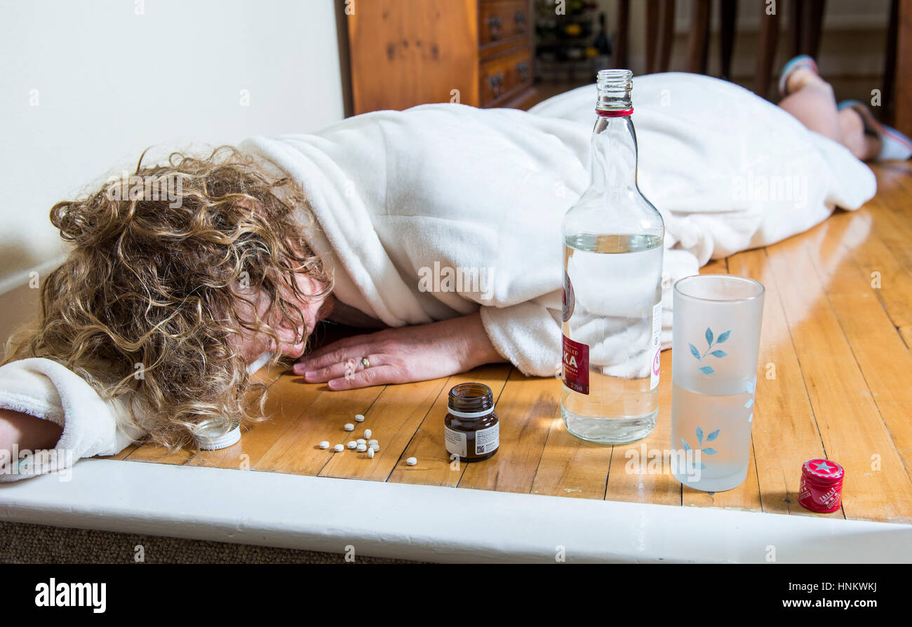 Depressed woman in her dressing gown at home during daytime taking pills and heavily drinking to self medicate - Photograph posed by model Stock Photo