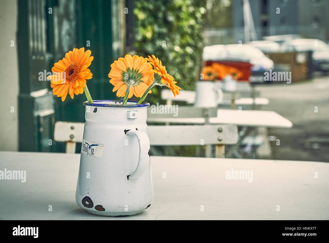 Orange Gerbera daisy flowers in a metal jug on a cafe table outside Stock Photo