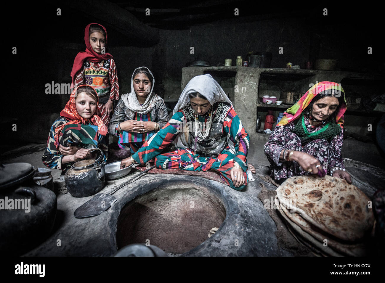 Afghanistan, Wakhan corridor, a group of women is preparing and baking bread in colorful traditional clothes, seated on the ground in stoned kitchen. Stock Photo