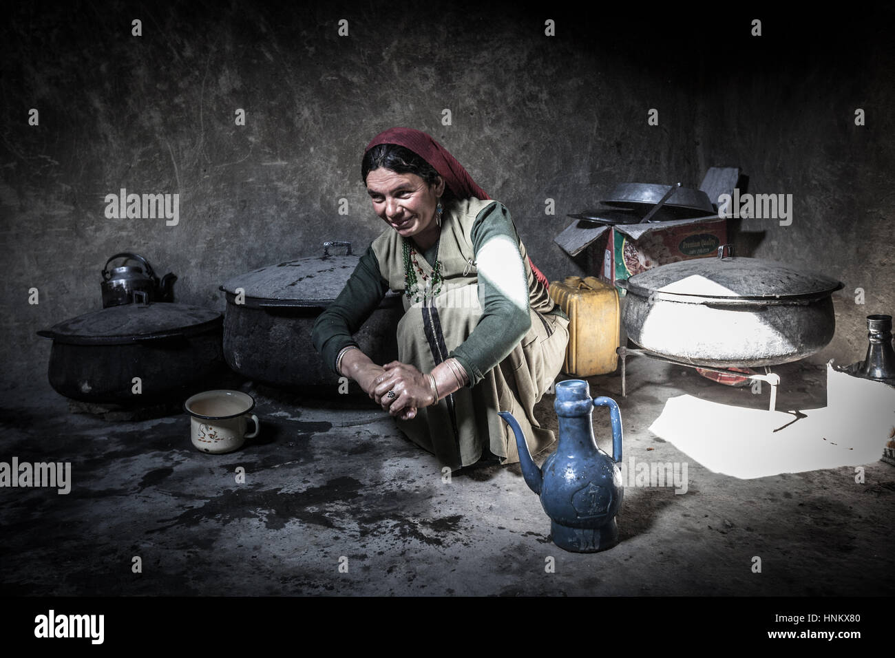 Afghanistan, Wakhan corridor,a woman is washing her hands in traditional clothes, seated on the ground in stoned kitchen. Stock Photo