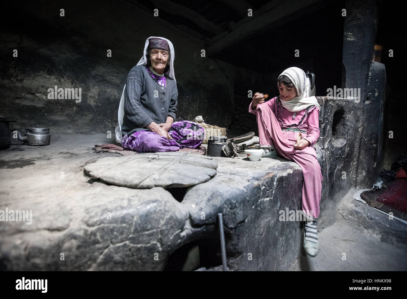 Afghanistan, Wakhan corridor, a nomad grandmother inside the house in the stone kitchen with child. Stock Photo