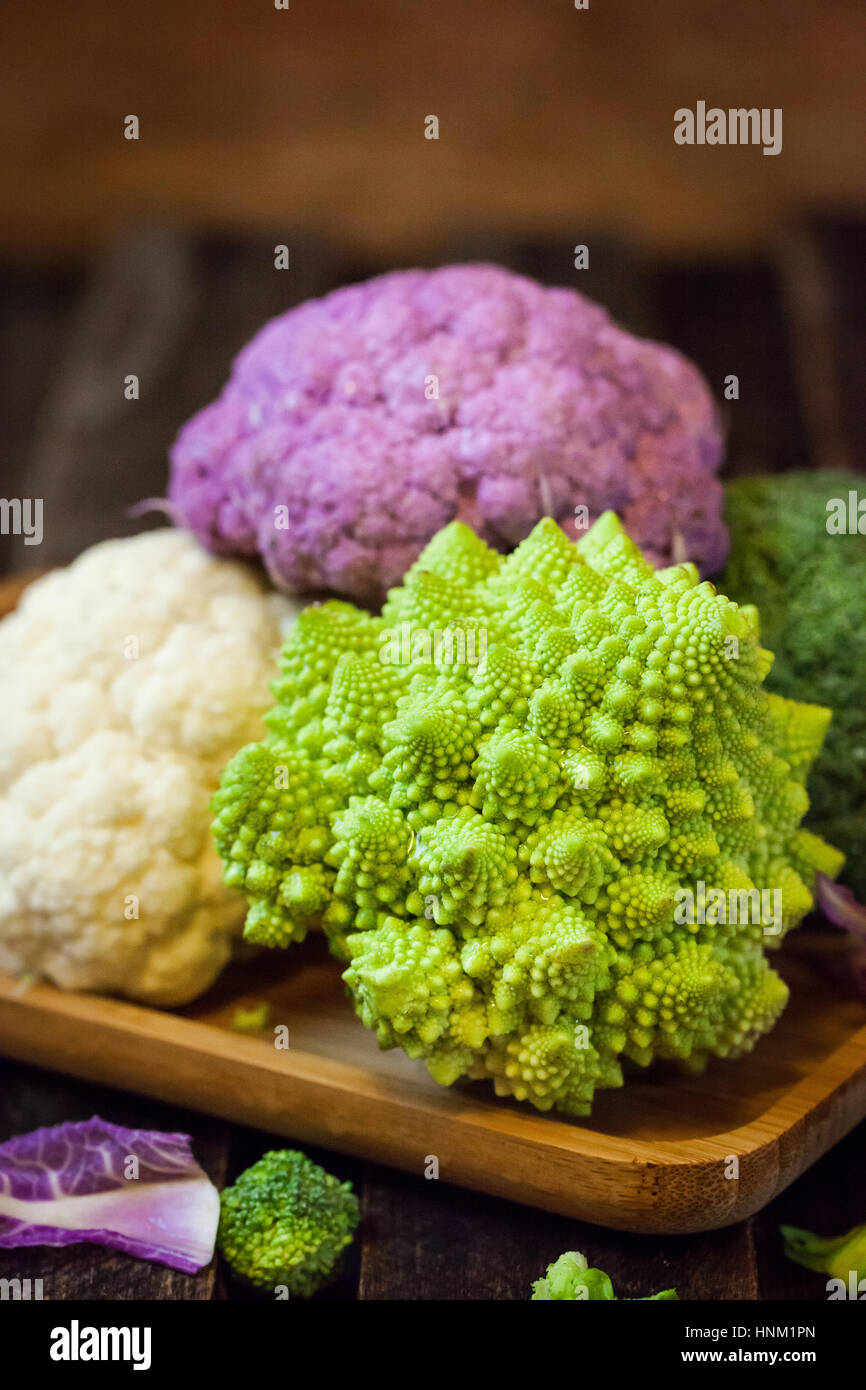 Fresh organic white and purple cauliflower, broccoli, romanesco in wooden bowl Stock Photo
