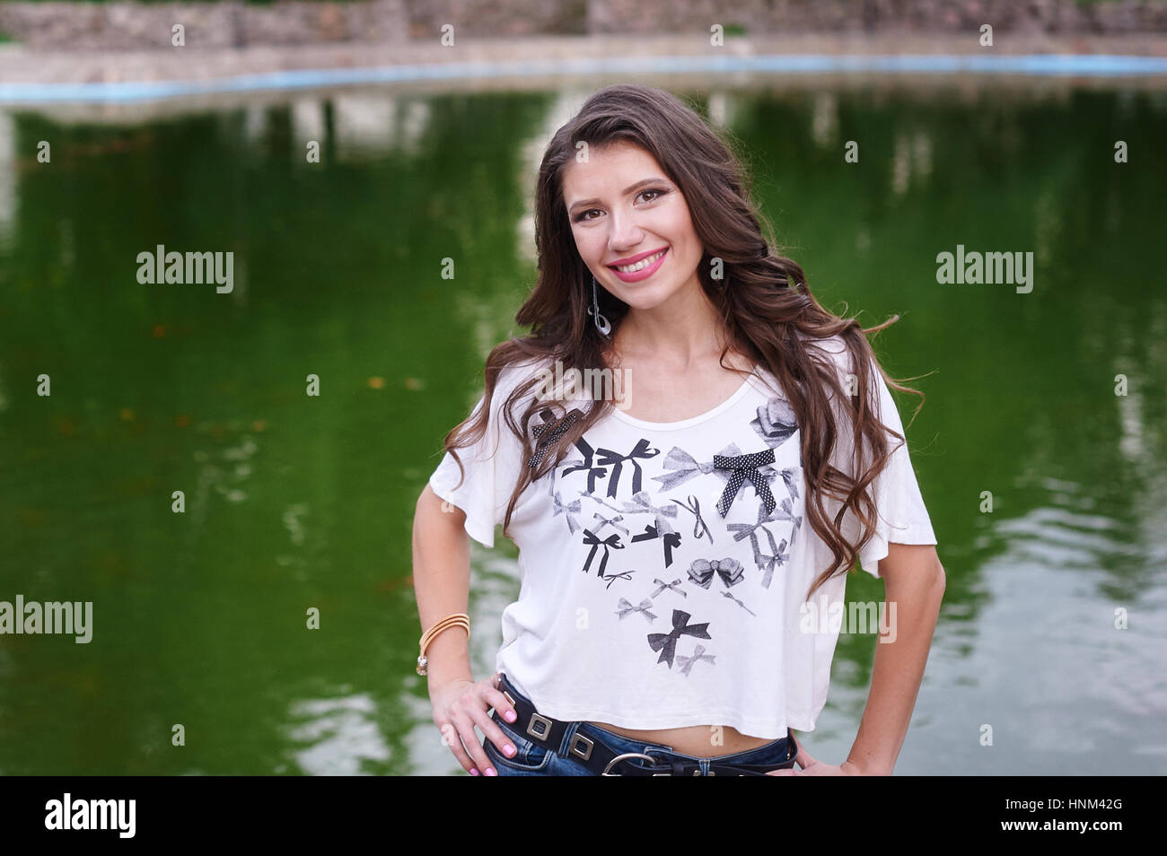smiling young woman standing on the background of the lake in the park Stock Photo